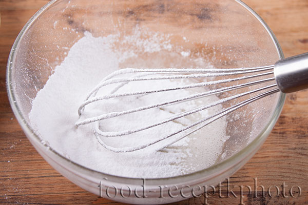 На фото белок и сахарная пудра в стеклянном салатнике для приготовления глазури
