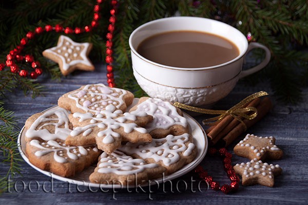 На фото имбирное печенье в белой тарелке и какао в белой чашке на фоне еловых ветвей