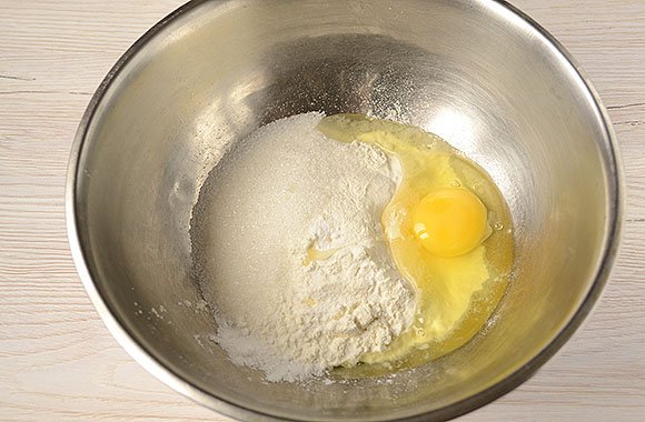 Сухие ингредиенты теста и куриное яйцо в металлической ёмкости