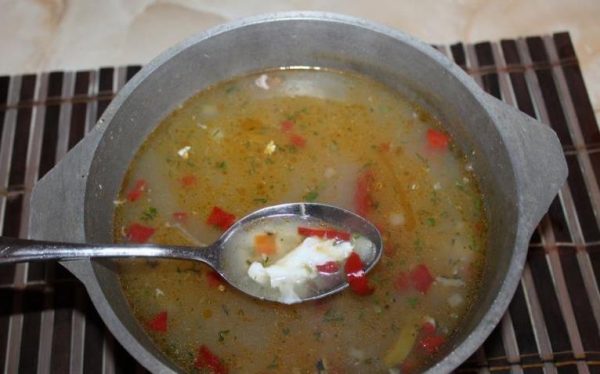 Кастрюля с супом и металлическая ложка с кусочком варёного яичного белка