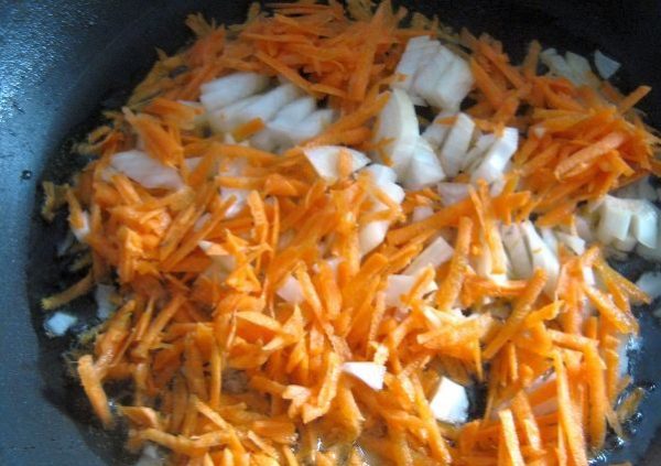 Тёртая морковь и маленькие кусочки репчатого лука в сковороде