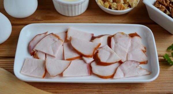 Нарезанная тонкими пластинами копчёная куриная грудка в белом прямоугольном салатнике на столе