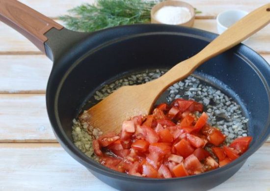 Обжаренный репчатый лук и нарезанные кубиками помидоры в сковороде с растительным маслом