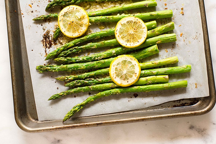 Close-Up of Asparagus topped with Parmesan Cheese on a Cookie Sheet Covered Pan After Roasting