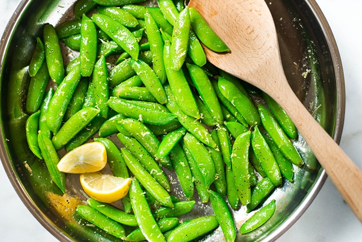 Sauteed sugar snap peas garnished with lemon slices ready to be served.