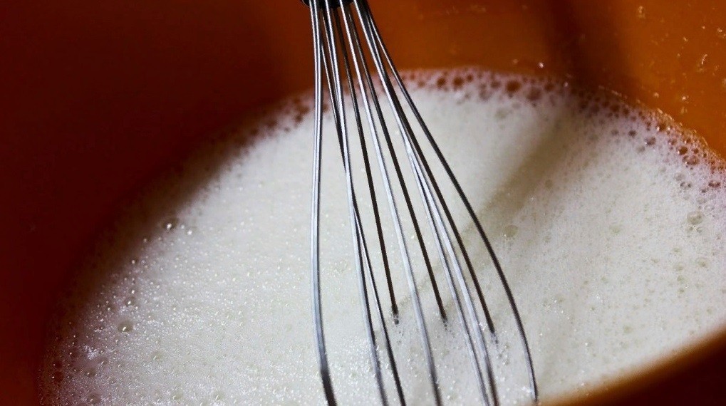 пенная яично-молочная масса в оранжевой миске с венчиком