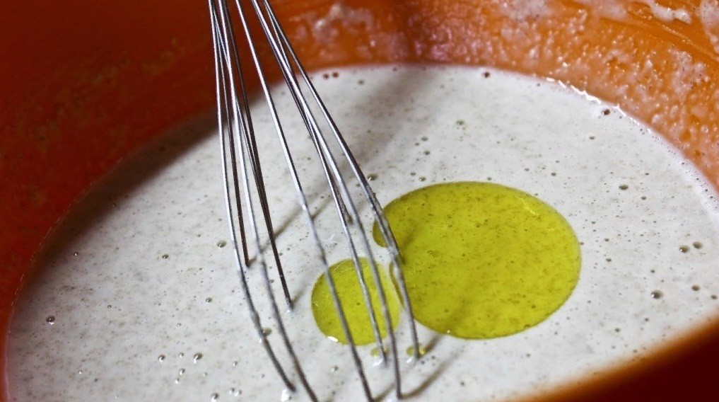 жидкое тесто с оливковым маслом в оранжевой миске в миксером