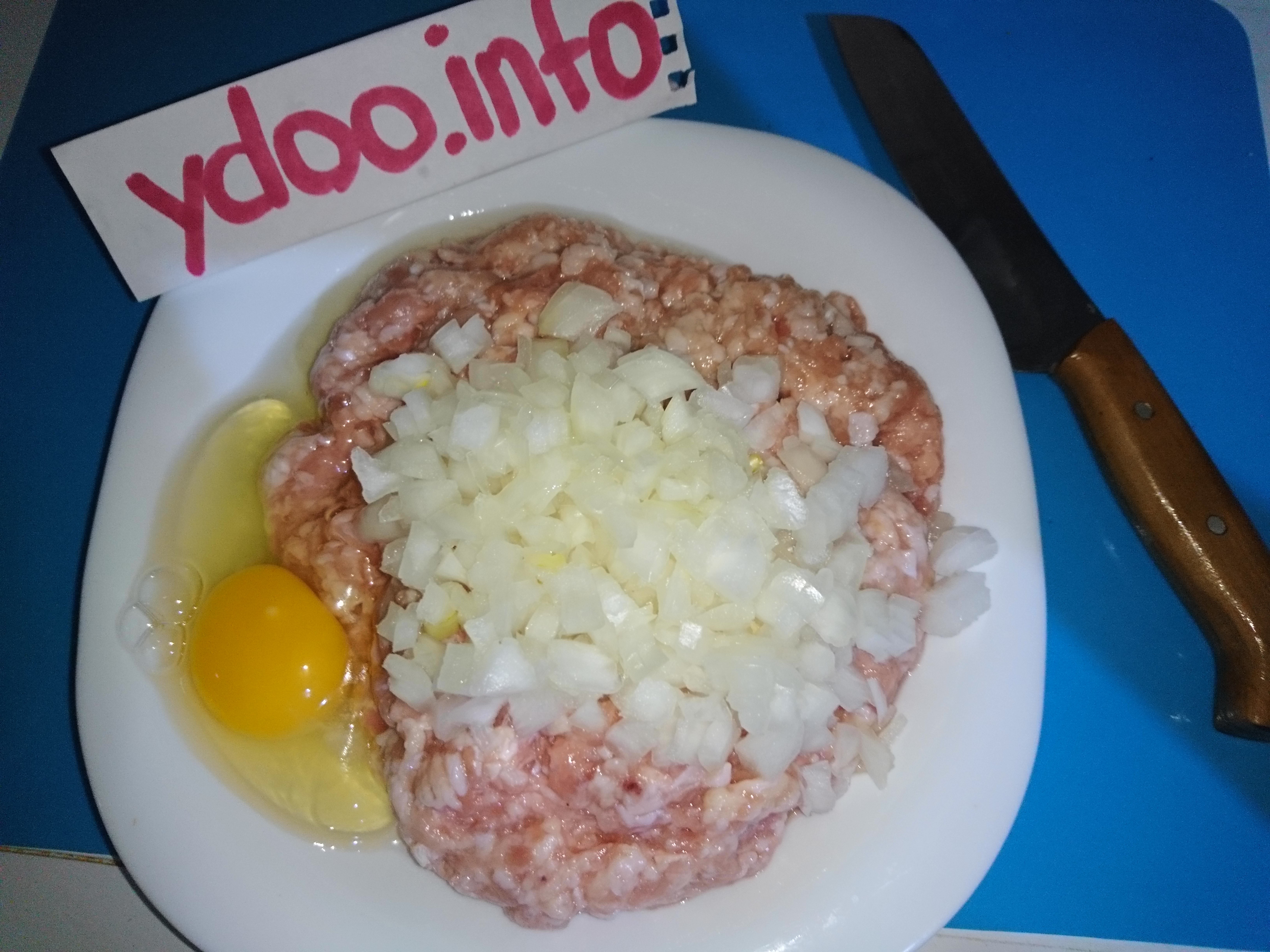 сырой куриный фарш с измельченным репчатым луком и яйцом в тарелке на столе