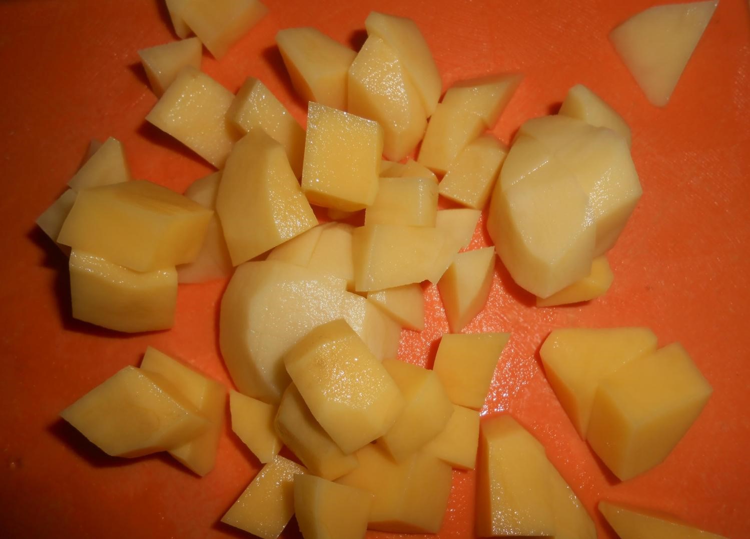 нарезанный кубиками сырой картофель на оранжевой разделочной доске
